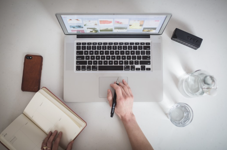 Person planning affiliate marketing strategies while working on a laptop, with a notebook and smartphone on the desk.